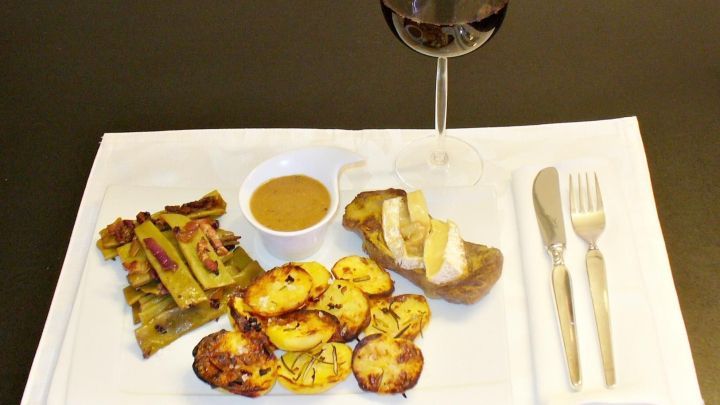 Ein zartes Entrecote liegt auf einem Teller mit knusprigen Speckbohnen und goldbraunen Kartoffelscheiben, umgeben von einem Glas Rotwein.