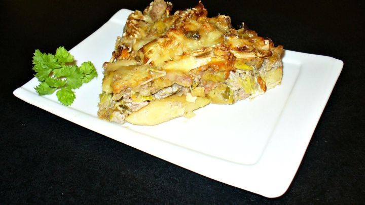 Ein St&uuml;ck &uuml;berbackener Porreetorte liegt auf einem wei&szlig;en Teller, umgeben von frischer Petersilie, auf einem dunklen Tisch.