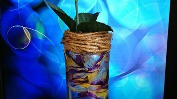 Eine dekorative, unifarbene Vase mit Nagellackmustern h&auml;lt eine rote Rose und steht vor einem farbigen, verschwommenen Hintergrund.