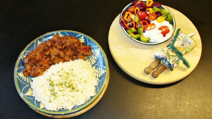 Ein kleiner Teller mit H&auml;hnchengyros liegt neben einer Sch&uuml;ssel mit frischem Salat und Joghurt, alles auf einem Tisch.