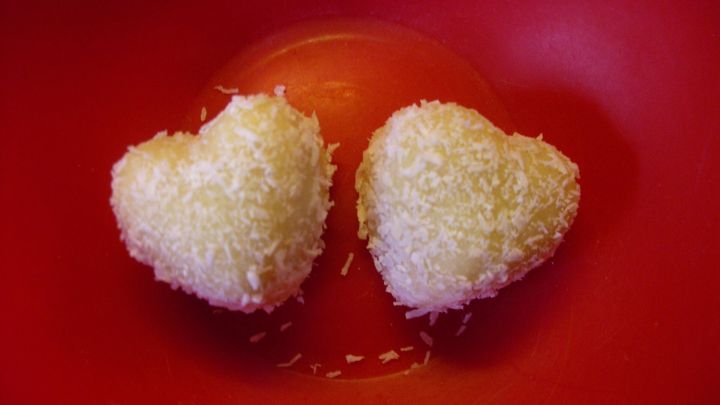 Herzf&ouml;rmige Mandel-Kokospralinen liegen in einer roten Schale und funkeln im Licht. Sie sind mit Kokosflocken &uuml;berzogen.