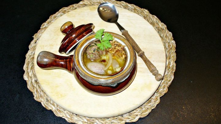 Eine rustikale Zwiebelsuppe wird in einem kleinen Tontopf serviert, garniert mit Petersilie, auf einem Holzuntersetzer.