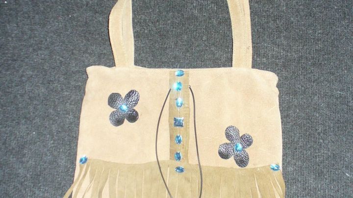 Schlichte Wildledertasche mit fransigen Details und Blumenstickerei h&auml;ngt vor einem grauen Hintergrund.