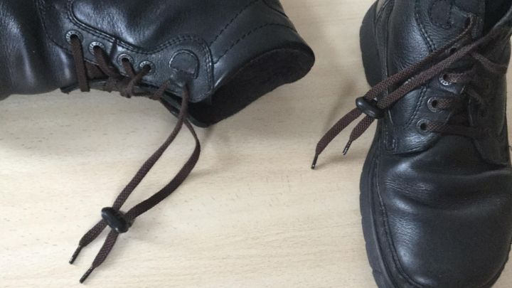 Schwarze Schuhe liegen auf einem Tisch, w&auml;hrend die Kordeln mit einem Kordelstopper sicher gebunden sind.