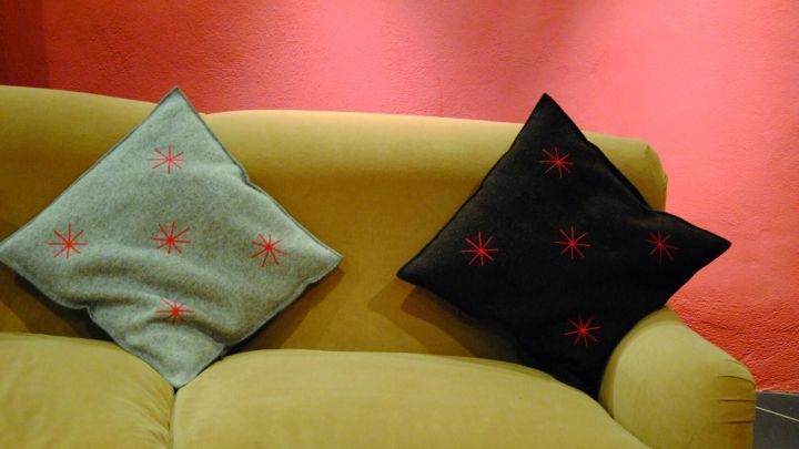 Ein gelbes Sofa mit zwei Kissen, einem gr&uuml;nen und einem schwarzen, steht vor einer rot gestrichenen Wand.