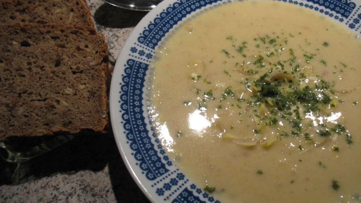 Eine cremige Chicoree-Suppe in einer blauen Sch&uuml;ssel, serviert mit dunklem Brot auf einem Tisch.