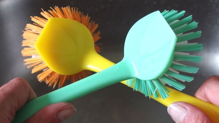 Bunte Geschirrsp&uuml;ler-B&uuml;rsten liegen in H&auml;nden, w&auml;hrend sie f&uuml;r das Geschirrsp&uuml;len in einer Sp&uuml;le vorbereitet werden.