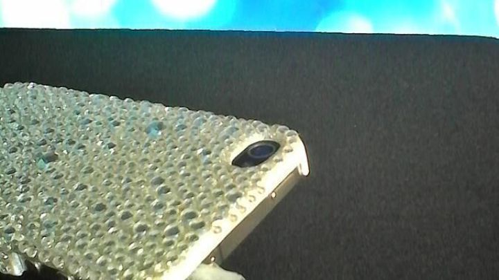 Ein Smartphone mit einer glitzernden H&uuml;lle hat einen Kopfh&ouml;reranschluss, in den ein Kabel eingef&uuml;hrt ist, vor einem blauen Hintergrund.