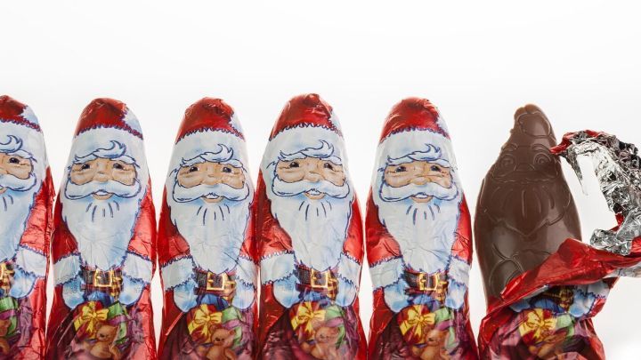 Sechs Schokoweihnachtsm&auml;nner stehen in Reihe, w&auml;hrend einer bereits ge&ouml;ffnet und teilweise gegessen wurde.