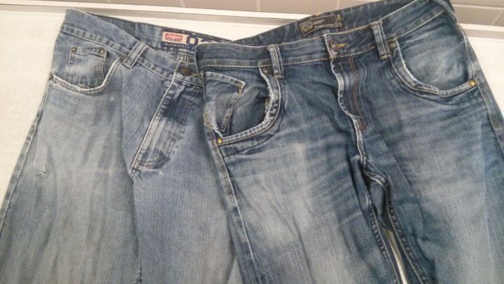 Ausgeblichene Jeans liegen nebeneinander auf einer hellen Oberfl&auml;che, zeigen unterschiedliche Verf&auml;rbungen und Waschspuren.