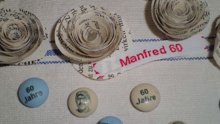Schlichte Tischdeko mit Papierrosen und Buttons, die f&uuml;r den Geburtstag von Manfred mit "60 Jahre" dekoriert sind.