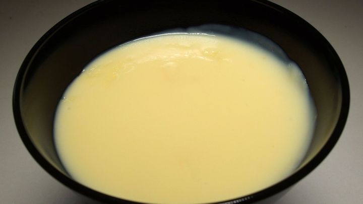 Ein schwarzes Sch&uuml;sselchen h&auml;lt cremigen T&uuml;tenpudding, der glatte, geleeartige Konsistenz zeigt, vor neutralem Hintergrund.