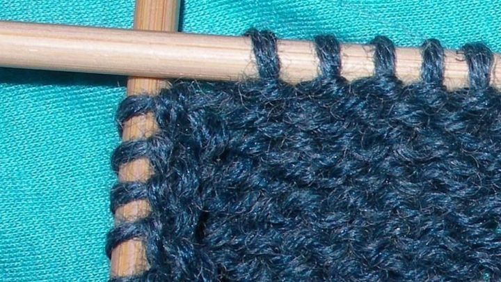 Holz-Nadeln halten einen dunkelblauen Strickfaden in der N&auml;he einer strahlend gr&uuml;nen Oberfl&auml;che, w&auml;hrend Runden gestrickt werden.