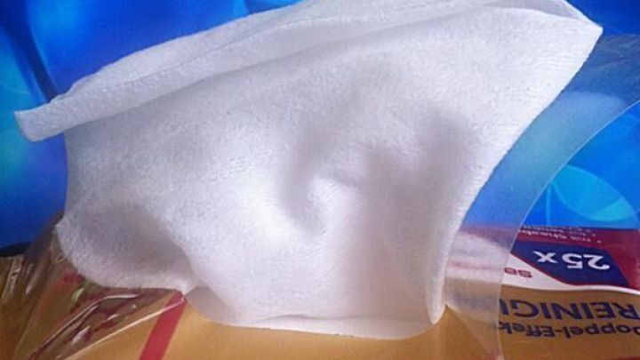 Ein wei&szlig;es, feuchtes Reinigungstuch liegt auf einer Packung, umgeben von einem blauen, blasenf&ouml;rmigen Hintergrund.