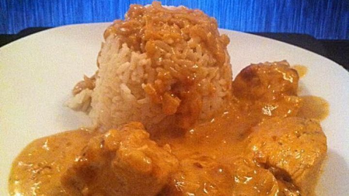 H&uuml;hnerbrustfilet liegt in cremiger Zwiebelrahmso&szlig;e, serviert mit lockerem Reis auf einem wei&szlig;en Teller.