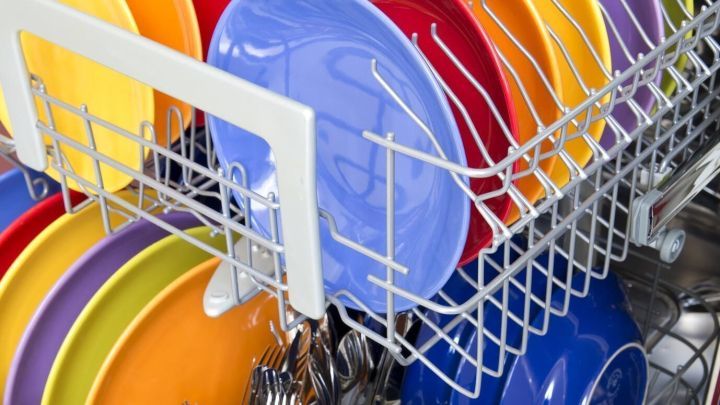 Bunte Teller und Besteck sind ordentlich in einer Sp&uuml;lmaschine platziert, bereit zum Reinigungsvorgang.