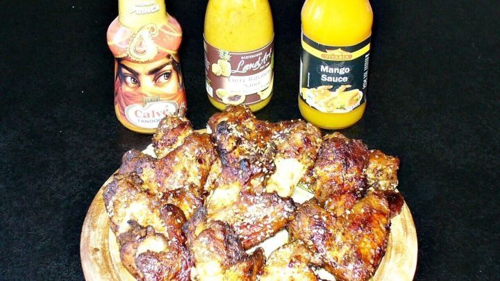 Marinierte gebackene H&auml;hnchenfl&uuml;gel liegen auf einem Teller, umgeben von verschiedenen So&szlig;enflaschen auf einem Tisch.