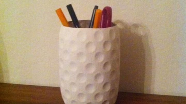 Ein wei&szlig;er Utensilienbeh&auml;lter steht auf einem Holzregal und h&auml;lt bunte Stifte und Marker in einem schlichten Raum.