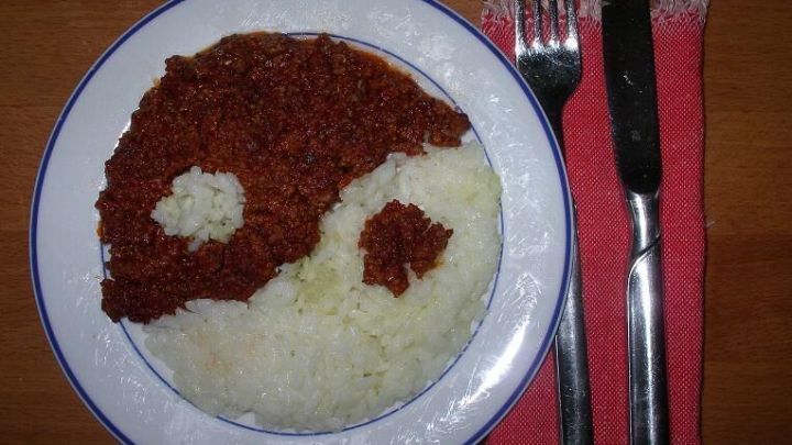Ein Teller mit Reis und einer Sauce, die in Form des Yin-Yang-Symbols angerichtet ist, liegt auf einem Tisch mit Besteck.