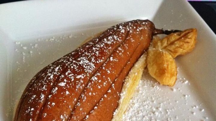 Ein gef&uuml;llter Bl&auml;tterteig sieht aus wie eine Birne und liegt auf einem wei&szlig;en Teller, umgeben von Puderzucker.