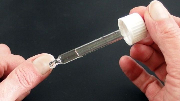 Eine Pipette mit Wasserstoffperoxid wird auf einen Nagel angewendet, um Nagelpilz zu behandeln. Der Hintergrund ist schwarz.