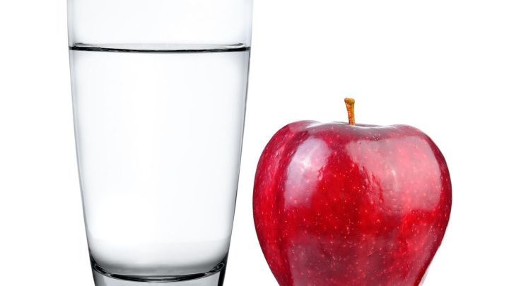 Ein Glas mit Wasser steht neben einem roten Apfel, symbolisch f&uuml;r regelm&auml;&szlig;iges, nat&uuml;rliches Abf&uuml;hren und gesunde Ern&auml;hrung.