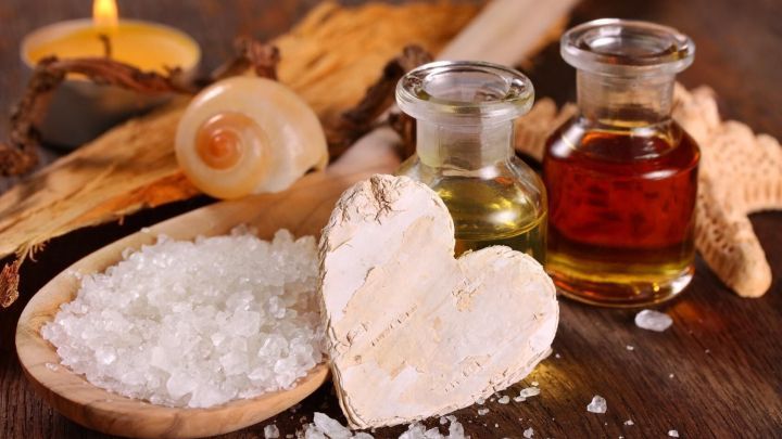 Ein Holzl&ouml;ffel kombiniert in einer gem&uuml;tlichen Umgebung mit Salzkristallen, &Ouml;len und einem Kerzenlicht f&uuml;r K&ouml;rperpeeling.