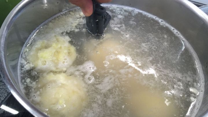 Kartoffelkn&ouml;del schwimmen in sprudelndem Wasser, w&auml;hrend jemand mit einer K&uuml;chenhilfe sie vorsichtig wendet.