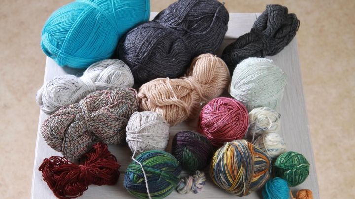 Bunte Wollreste liegen chaotisch auf einem Tisch, ideal zum Verwerten f&uuml;r kreative Handarbeiten und DIY-Projekte.
