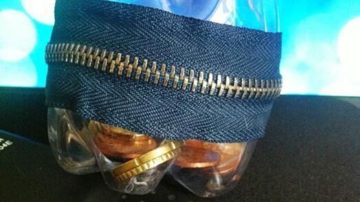 Ein wiederverwendeter Beh&auml;lter aus einer Plastikflasche, umh&uuml;llt von Jeansstoff, steht auf einem dunklen Tisch.