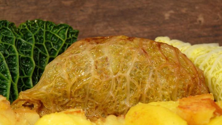 Ein knuspriger Wirsingwickel liegt appetitlich neben goldenen, gebratenen Kartoffeln und frischem Wirsing auf einem Holzbrett.
