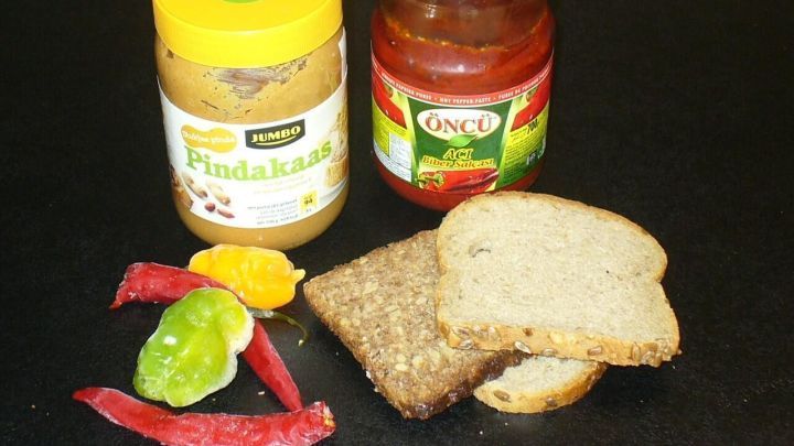 Ein Erdnuss-Chili-Brot-Snack liegt auf einem schwarzen Untergrund. Die Brotscheiben sind mit Erdnussbutter und Chili-Sauce umgeben.