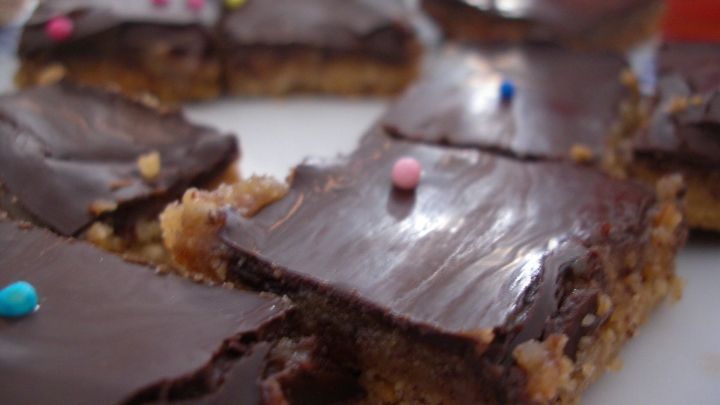 Schokoladige Venusschnitten liegen auf einem Teller, mit gl&auml;nzender Karamell-Schicht und bunten Streuseln dekoriert.