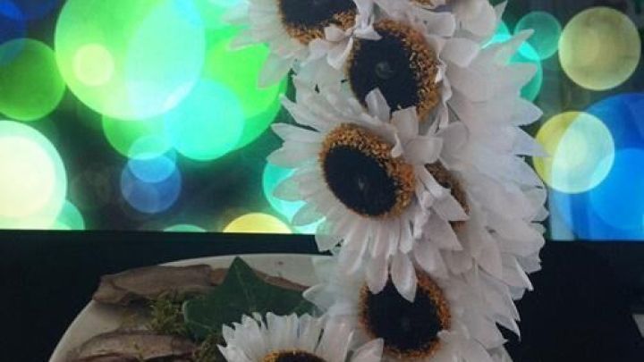 Tasse gie&szlig;end: Wei&szlig;e Kunstblumen flie&szlig;en aus einer schwebenden Tasse auf einen Teller, umgeben von Moos und Rinde.