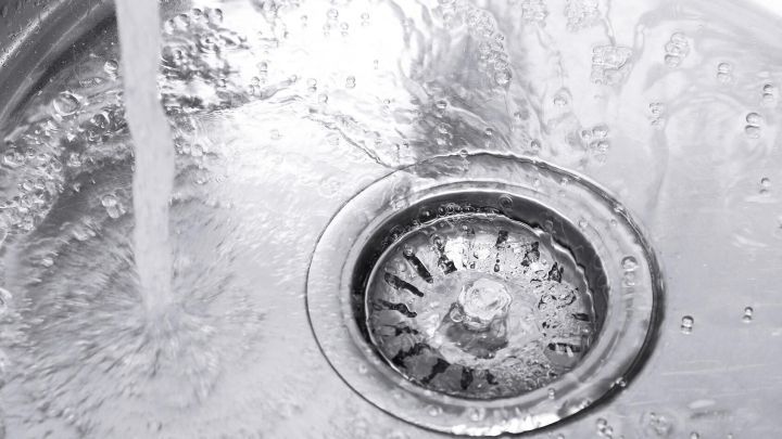 Ein Abfluss im Waschbecken wird von str&ouml;mendem Wasser gesp&uuml;lt, w&auml;hrend er eine glatte, gl&auml;nzende Oberfl&auml;che zeigt.