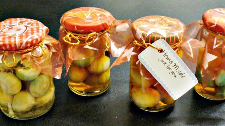 Gl&auml;ser mit eingelegtem Knoblauch und Weinbrand stehen ordentlich auf einem Tisch, dekoriert mit bunten Deckeln und Etiketten.