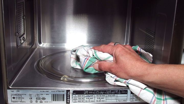 Eine Hand wischt mit einem Geschirrtuch die Innenfl&auml;che einer Mikrowelle, um Essigger&uuml;che zu beseitigen.
