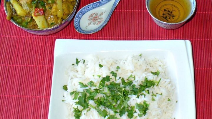 Ein H&uuml;hnerfrikassee liegt in einer Sch&uuml;ssel, w&auml;hrend daneben frisch gekochter Koriander-Reis auf einem Teller serviert wird.