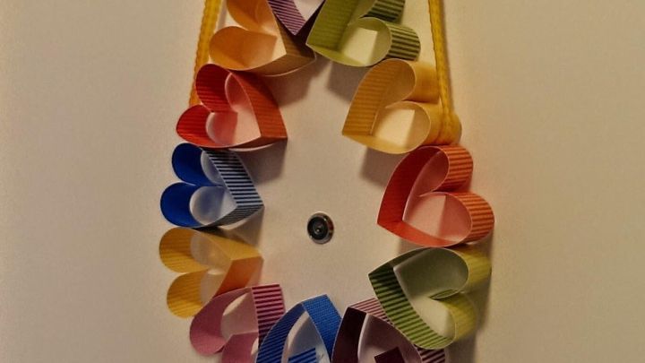 Ein bunter T&uuml;rkranz aus Papierherzen h&auml;ngt an gelber Schnur an einer Wand, perfekt f&uuml;r Ostern. Er strahlt Freude aus.