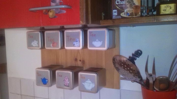 An der Wand ist ein Regal mit Teedosen und Kaffeepads, die ordentlich aufgereiht sind und den K&uuml;chenraum strukturieren.