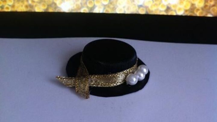 Ein kleines H&uuml;tchen liegt auf wei&szlig;em Papier, dekoriert mit einem goldenen Band und Perlen, vor einem glitzernden Hintergrund.