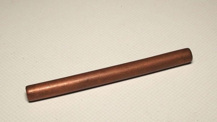 Ein gl&auml;nzendes Kupferobjekt liegt auf einer neutralen Oberfl&auml;che, ideal zur Anwendung von Zahnpasta zur Reinigung.