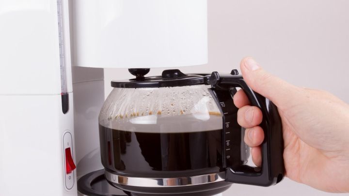 Eine Kaffeemaschine mit digitaler Zeitschaltuhr br&uuml;ht frisch gebrauten Kaffee, w&auml;hrend eine Hand die Kanne h&auml;lt.