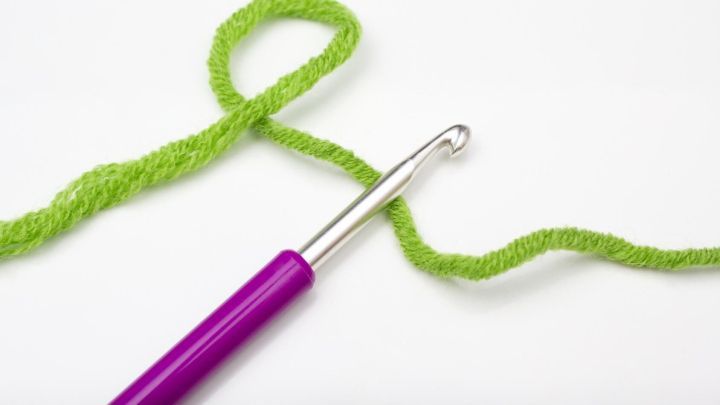 Eine H&auml;kelnadel mit einem lila Griff liegt neben einem gr&uuml;nen Garn, das lose gewickelt ist, bereit zum Stopfen von Laufmaschen.