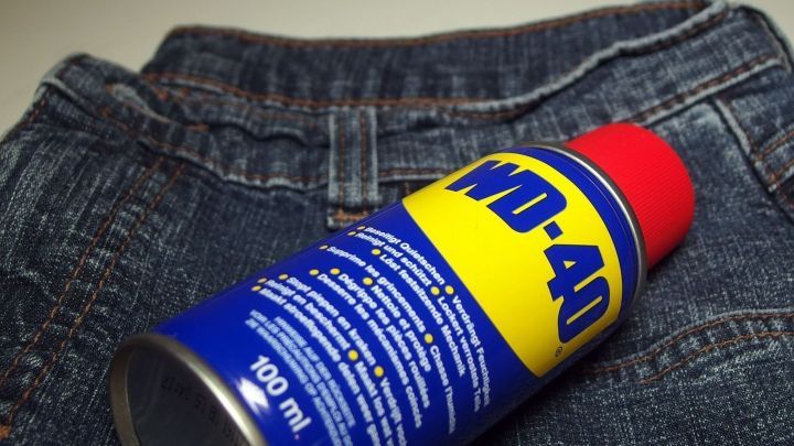 Eine Spraydose mit WD-40 liegt auf einer Jeans, bereit zu werden gebraucht, um Harz oder Pech zu entfernen.