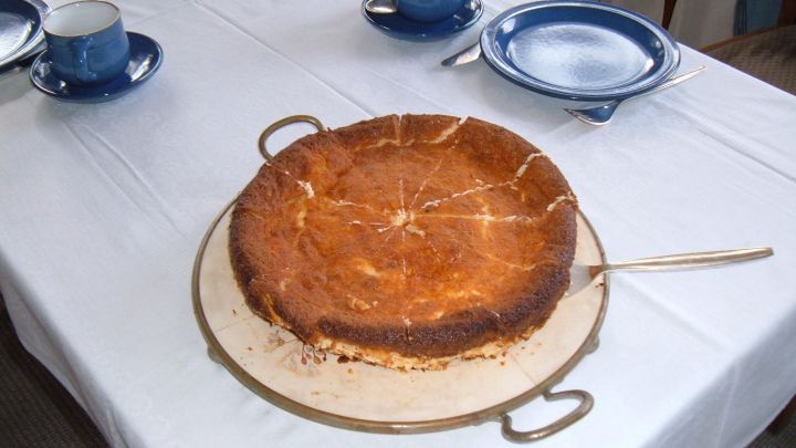 Ein goldbrauner Eierschecke-Kuchen steht auf einem Tisch, umgeben von blauen Tellern und Tassen.
