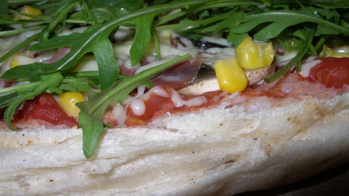 Eine frisch belegte Pizza mit bunten Zutaten wie Rucola und Mais liegt auf einem Holzbrett, bereit zum Genie&szlig;en.