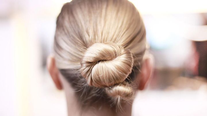 Eine blonde Frau tr&auml;gt einen eleganten Dutt, der sorgf&auml;ltig am Hinterkopf gesteckt ist, in einem hell beleuchteten Raum.