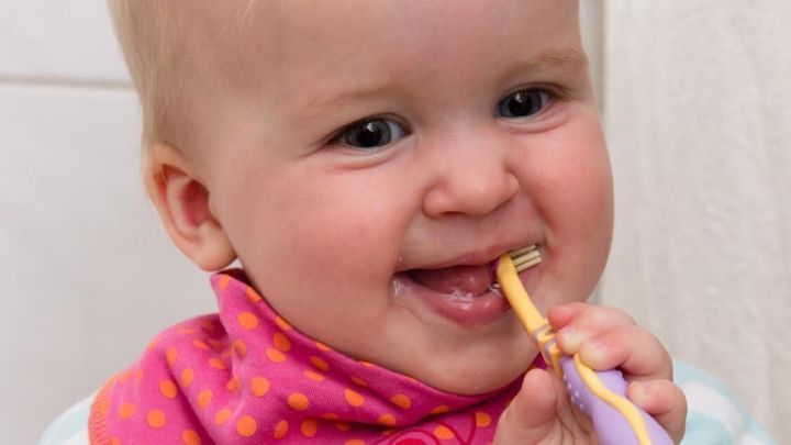 Ein l&auml;chelndes Kleinkind mit einem bunten L&auml;tzchen putzt begeistert seine Z&auml;hne in einem hellen Badezimmer.