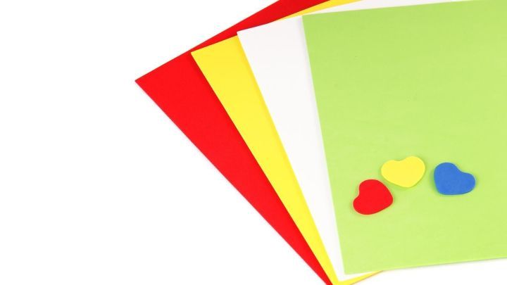 Verschiedene farbige Bastelpapiere liegen nebeneinander, w&auml;hrend bunte Herzchen auf der gr&uuml;nen Fl&auml;che arrangiert sind.